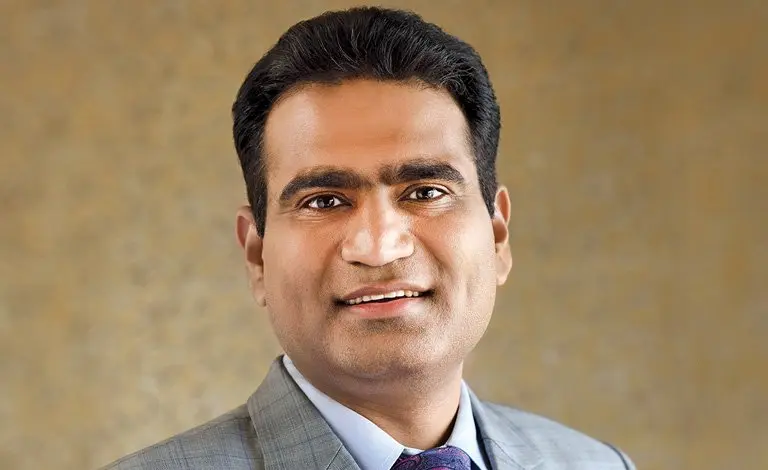 Professional portrait of a smiling man wearing a gray suit, white shirt, and tie against a neutral background
